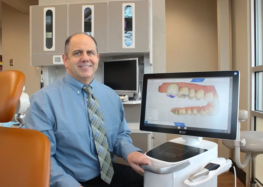 Dr. Slaman beside the Primescan unit, with a digital model of a patient's teeth on screen.